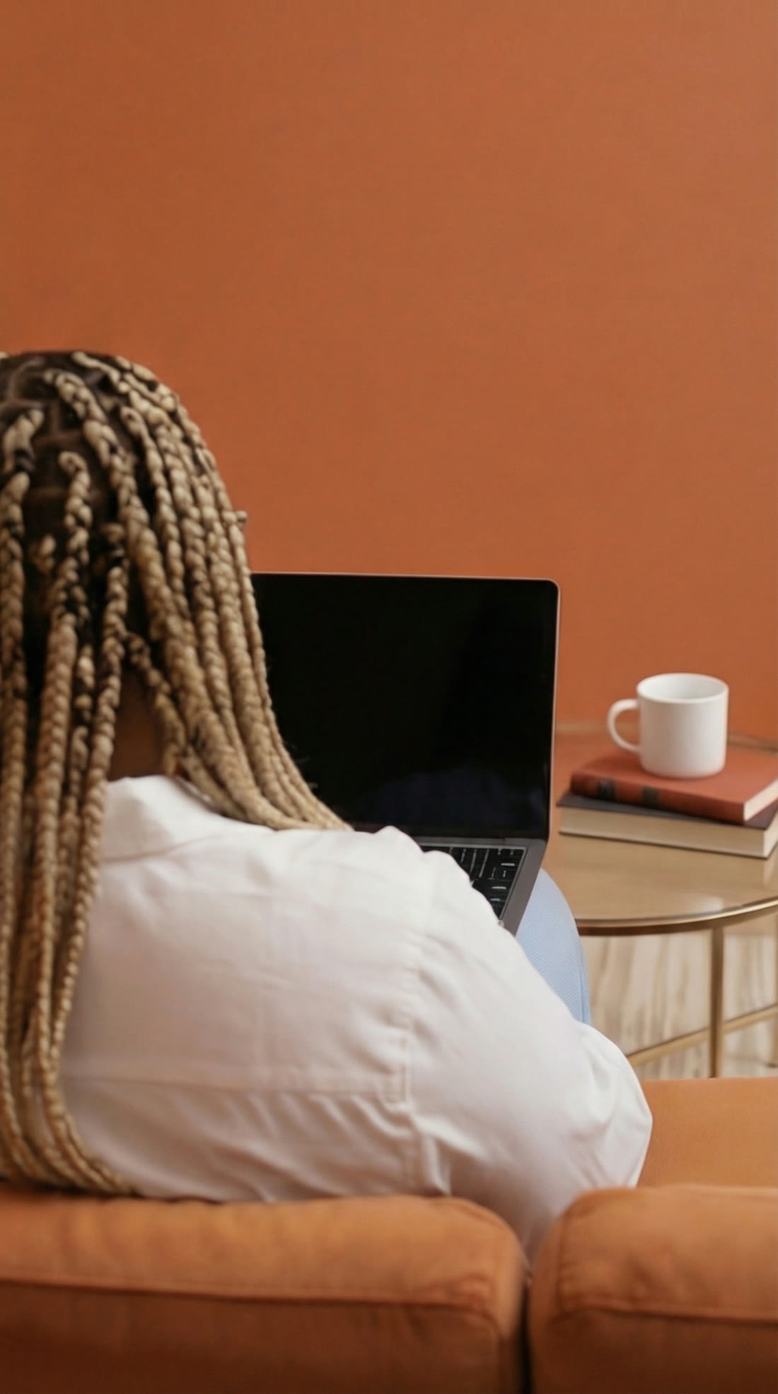 Tomi from behind, working on her laptop against an orange wall