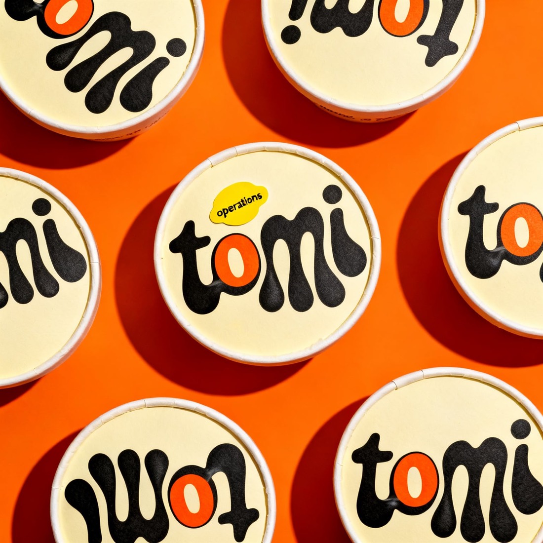 Round cream lids on an orange ground, each filled edge to edge with giant warped black tomi letters
